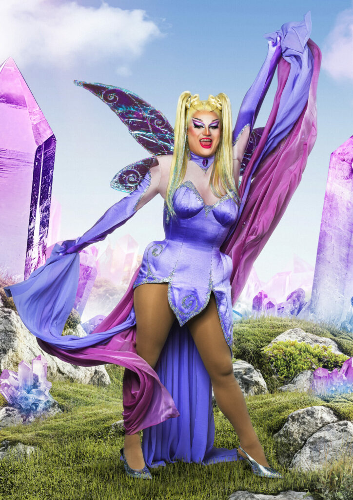 Drag queen in a purple petal mini dress, wearing a pink and purple cape and fairy wings