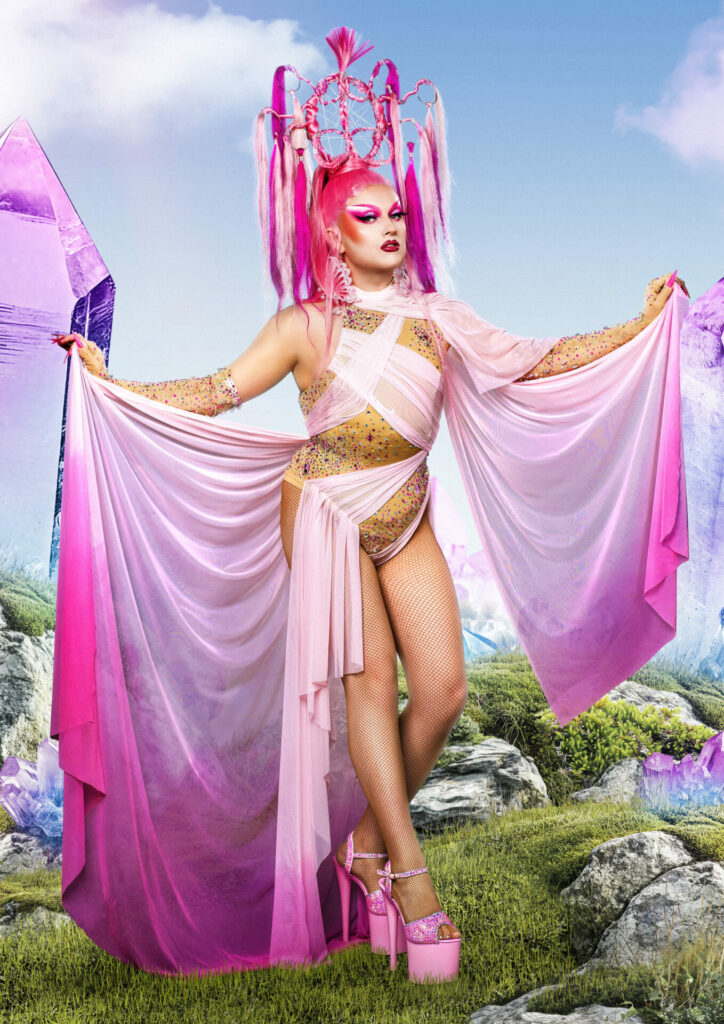 Drag queen draped in pink ombre fabric wearing a statuesque pink wig