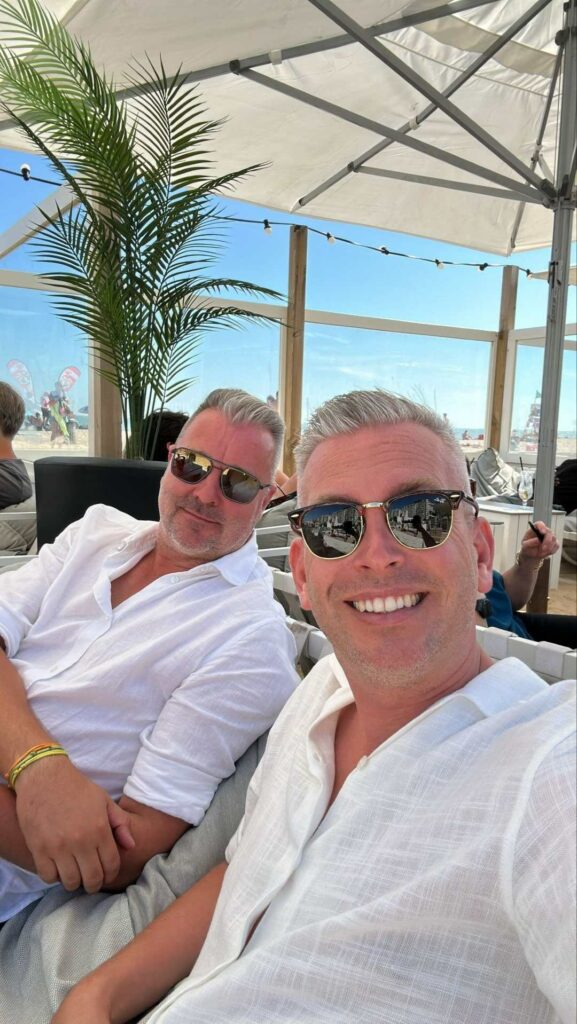 Two smiling men in white shirts wearing sunglasses