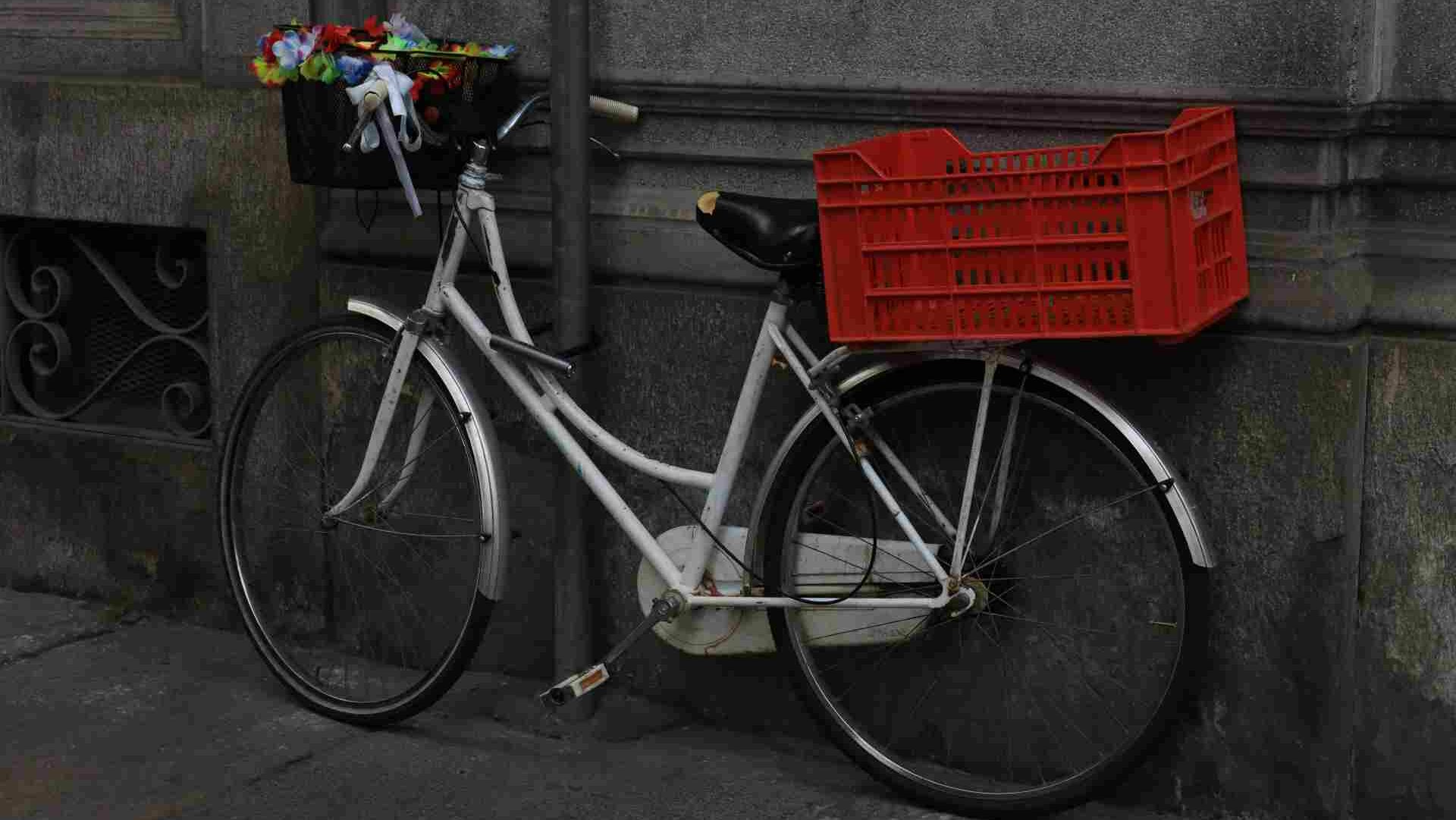 A biek with a red basket on the back of it standing against a wall