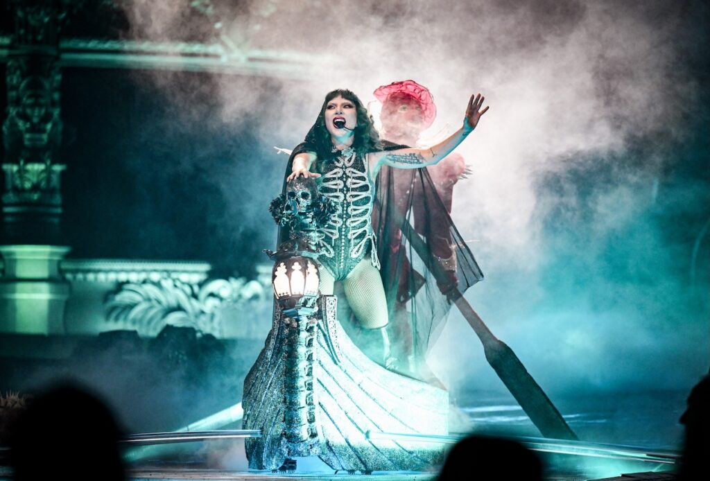 Lady Gaga with black hair on rowboat surrounded by dry ice, singing