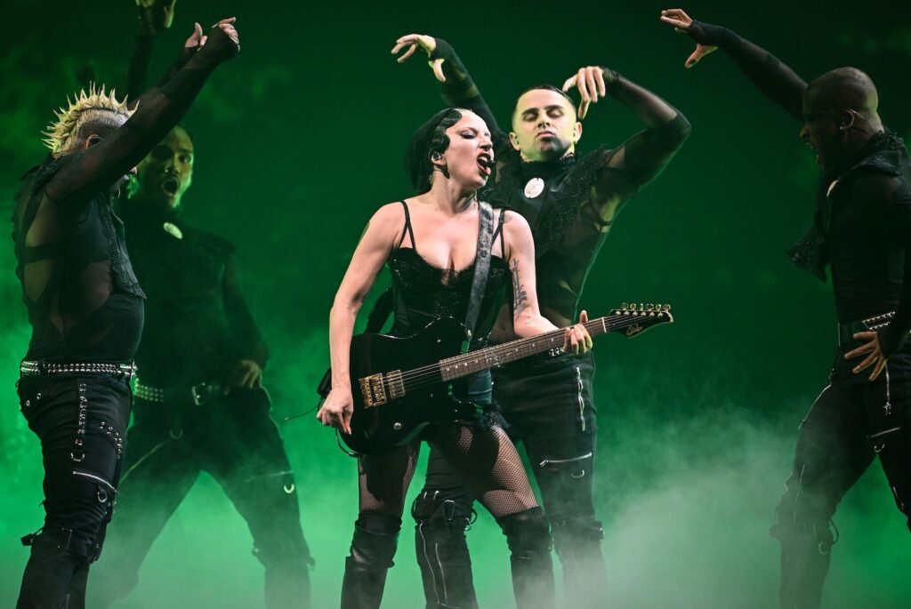 Lady Gaga in black corset with guitar and dancers, green background