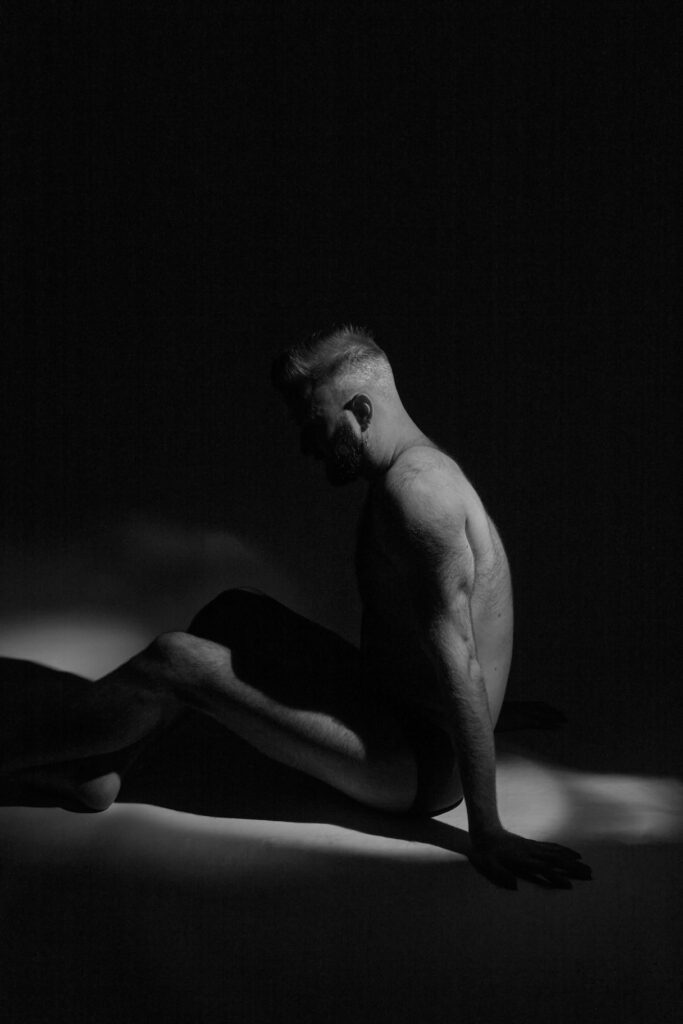 Black and white photo of a man sat upright just his underwear 