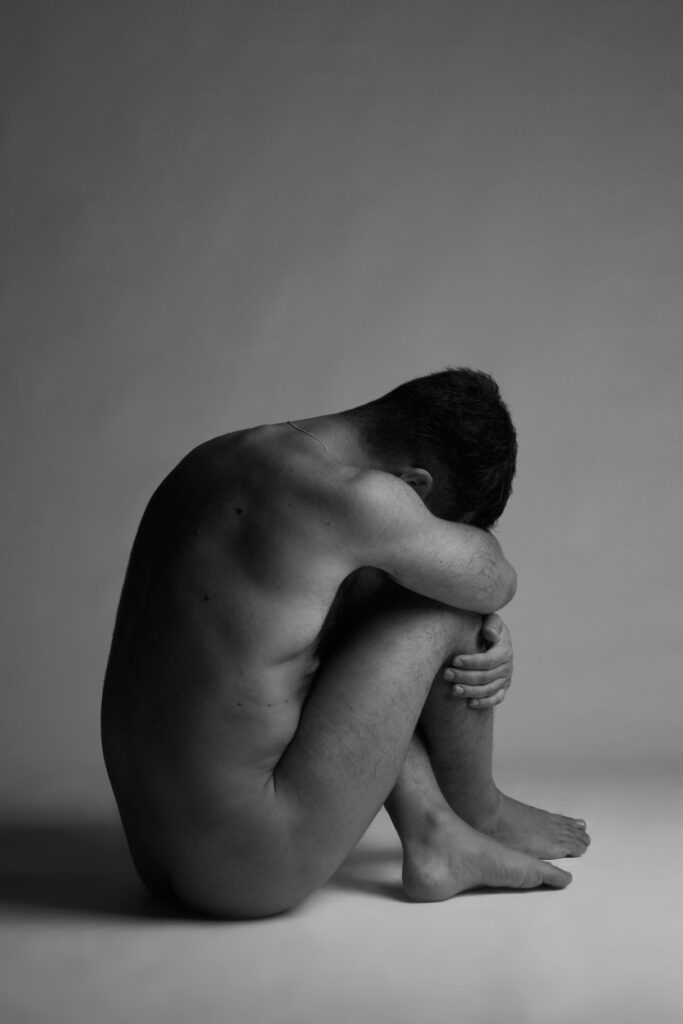 Black and white photo of a naked man with his head between his legs