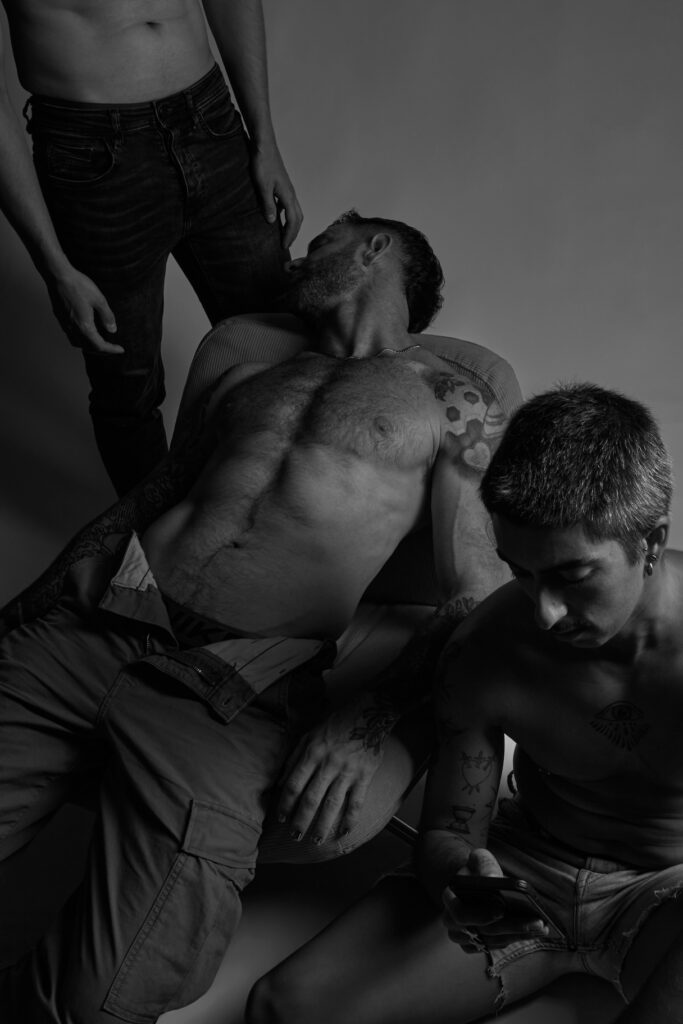 Three topless men sprawled out across one another