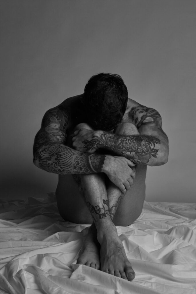 A naked man with his head between his legs 
