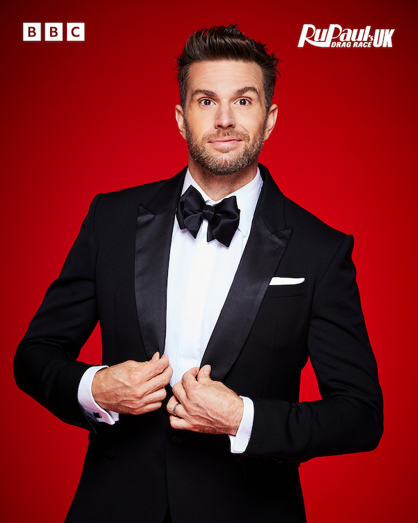 Joel Dommett wearing a smart black suit and tie