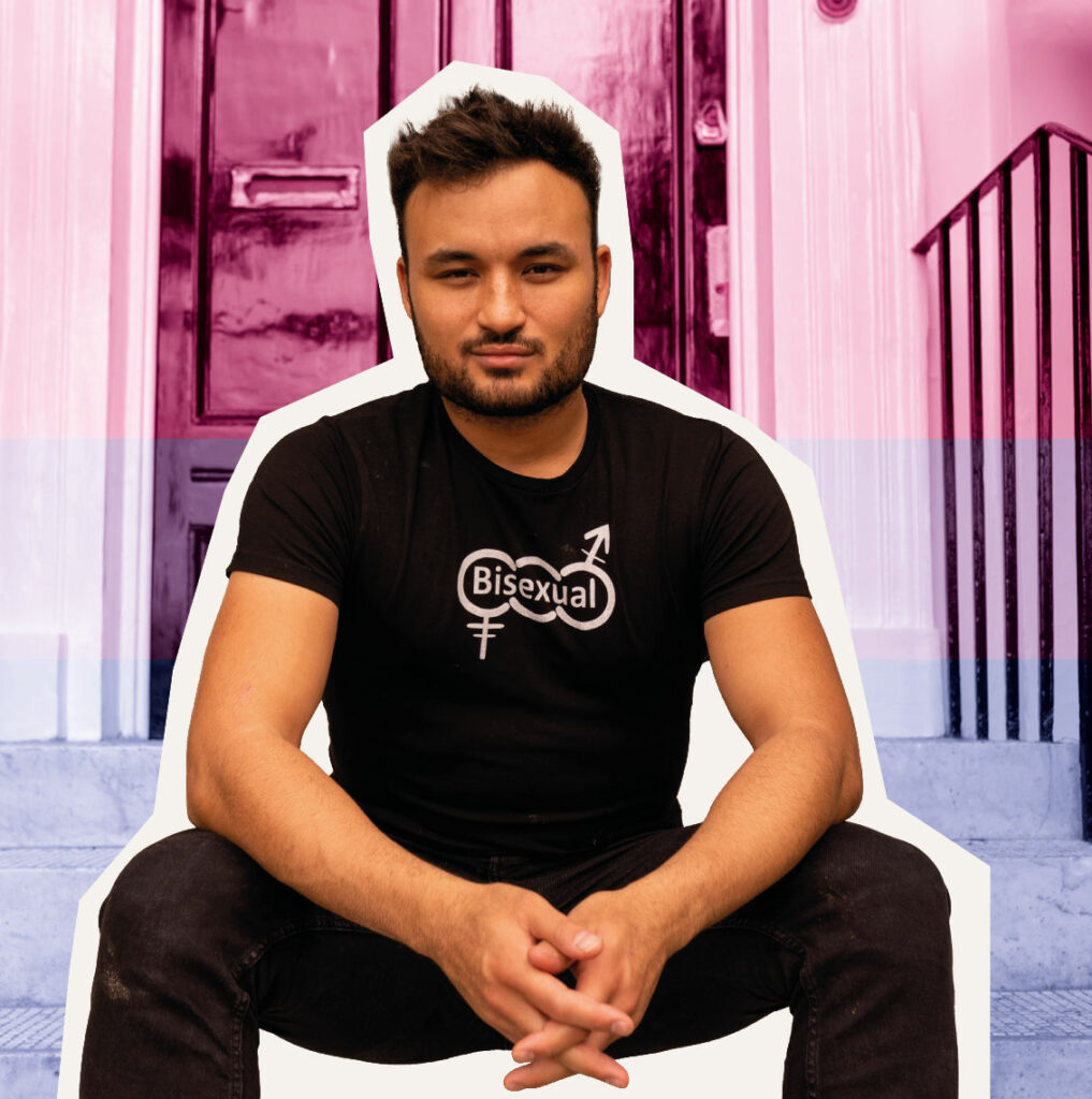 Lewis Oakley, broadcaster, author and father, also speaks to writer Florence Scordoulis for this feature - here, he is pictured sitting in black trousers and a black t-shirt with the word 'bisexual' on the front (Image: Lewis Oakley /Laurene Pineau-Taylor/Pexels/Unsplash/Getty)