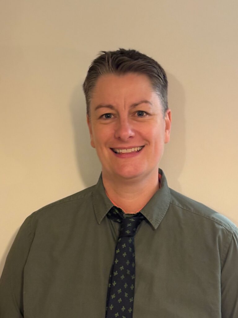 a head and shoulders shot of Counsellor Zoë Hughes in a green shirt and black patterned tie