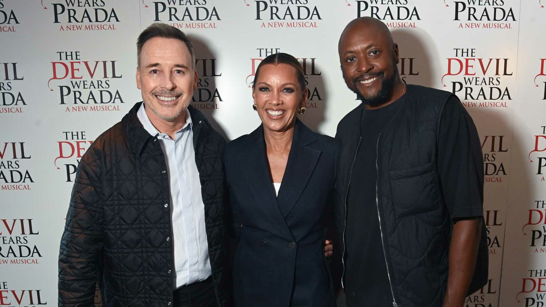 David Furnish, Vanessa Williams, Matt Henry standing in front of The Devil Wears Prada musical photo board
