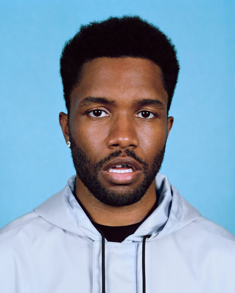 head and shoulders portrait shot of frank in grey coat against blue backdrop