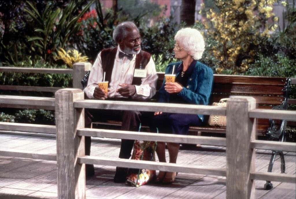 Two Golden Girls cast members sitting on a bench drinking coffee