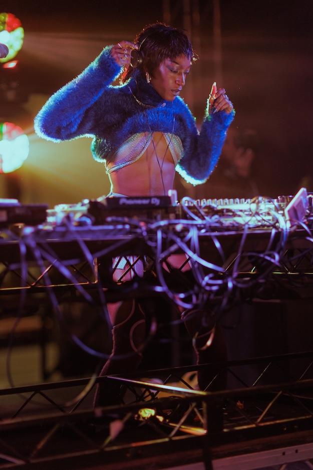 DJ wearing a blue jumper with their hands in the air