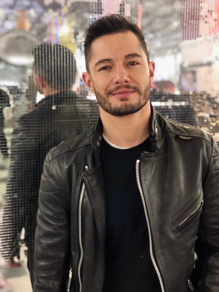 Jake Graf, beard, in a black leather jacket against a mirrorball-style flat backdrop