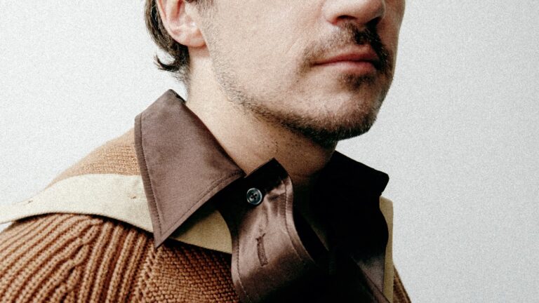A close-up of a model wearing brown collared knitwear from the Denzilpatrick Spring/Summer 2026 menswear lookbook.