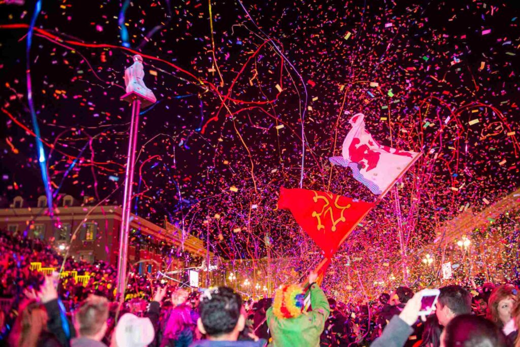 A night-time photo showing a large crowd of people celebrating the Lou Queernaval carnival in Nice, France.