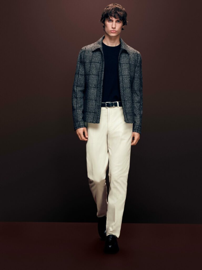 Male model walks a runway wearing a check work jacket and white trousers from the M&S Autograph Autumn/Winter 2025 collection.