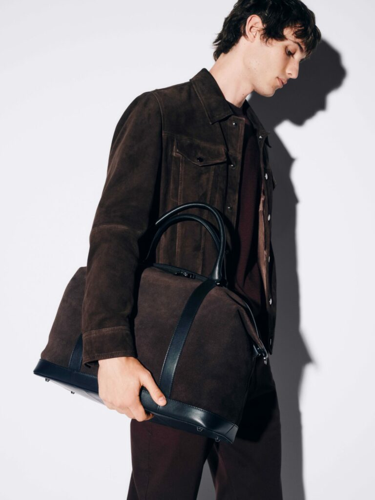 A male model wearing a suede jacket carries a matching suede weekender bag with leather details from the M&S Autograph Autumn/Winter 2025 collection.