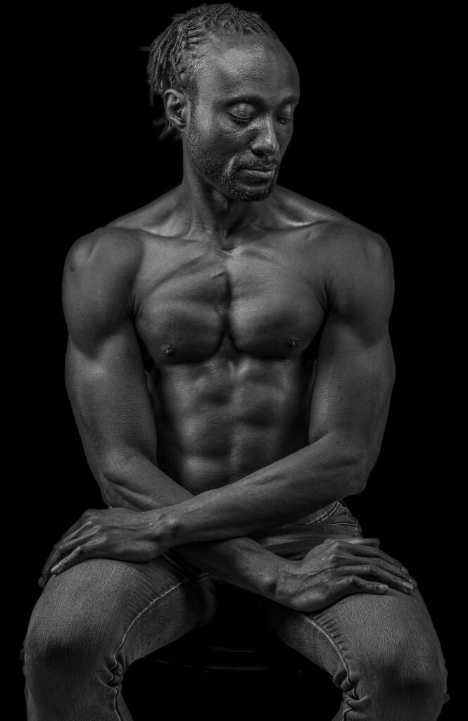 "A man sits in stillness, caught between who he once was and who he is becoming. Sharp light etches every line across his face, marking survival, grief, and reflection. This portrait shows midlife as transformation, where the heaviness of lived experience rests on his shoulders, yet carries within it the quiet potential of becoming someone new."