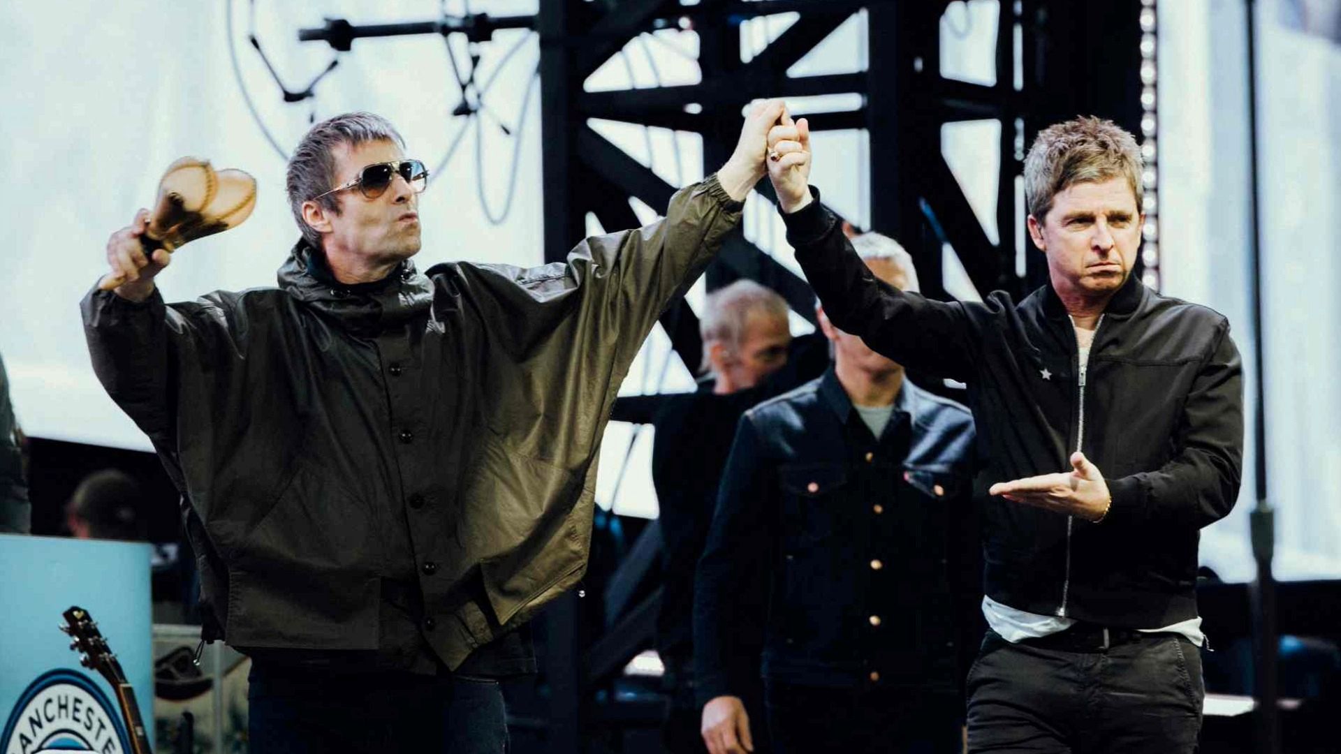 Liam and Noel Gallagher holding hands on stage at Wembley Stadium