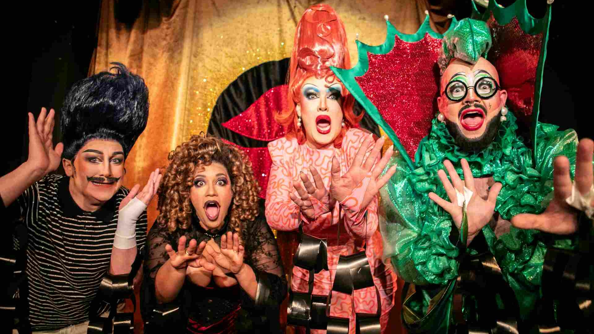 Four drag performers in flamboyant oufits posing on a theatre stage