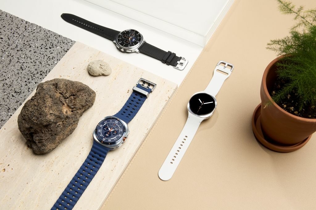 Three smart watches sitting on a desk with rocks and a plant by them