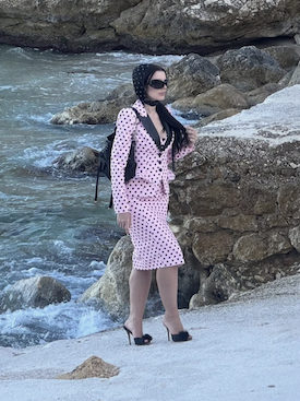 Juli Fox in a headscarf and pink and black blazer and skirt walking by the sea