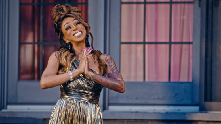 Tiffany Polard in a gold dress smiling and clasping hands together