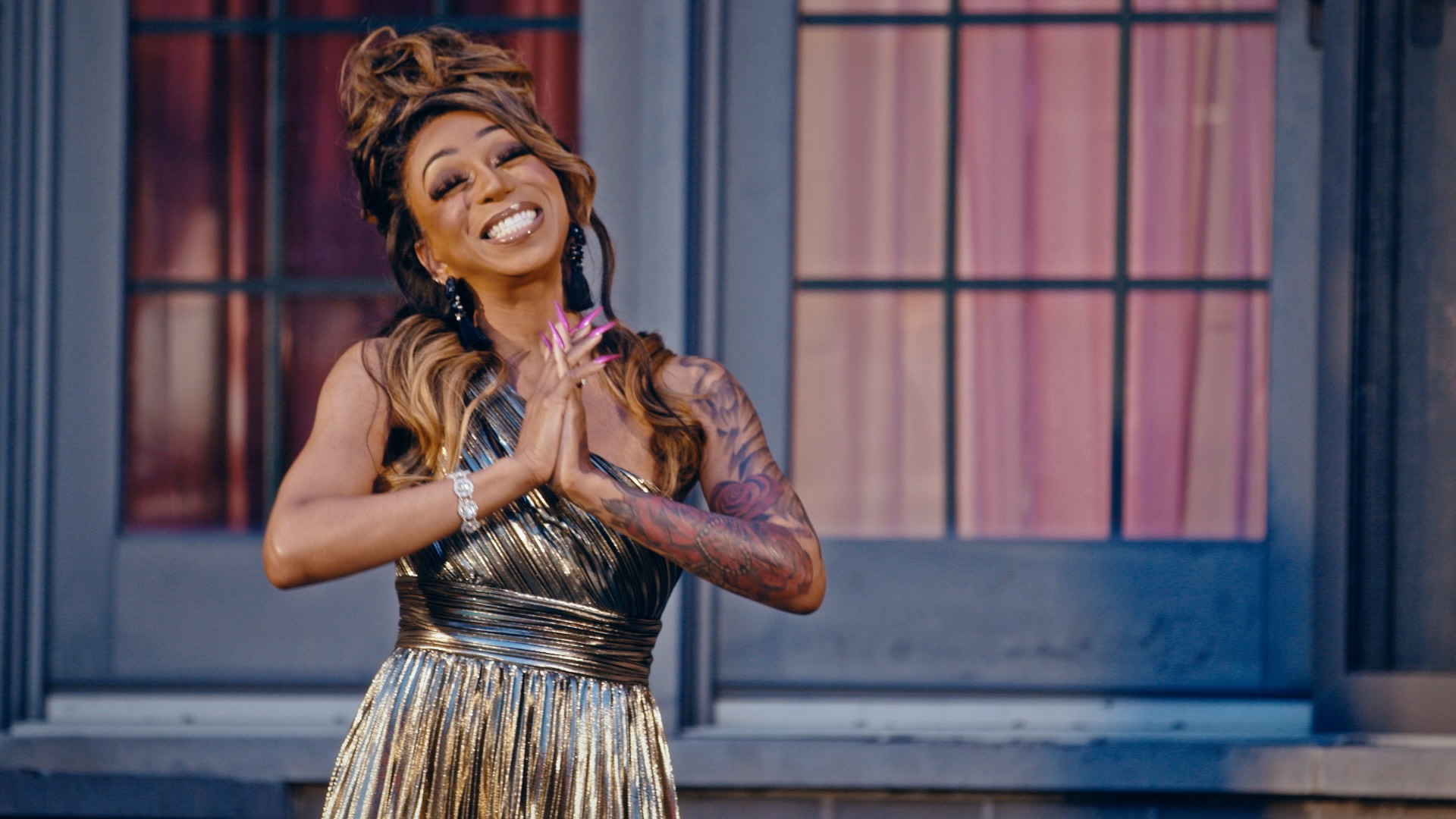 Tiffany Polard in a gold dress smiling and clasping hands together