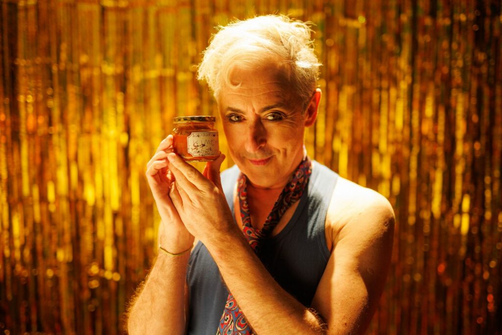 Alan Cumming holding a jar in a promo shot for his film Sleazy Tiger