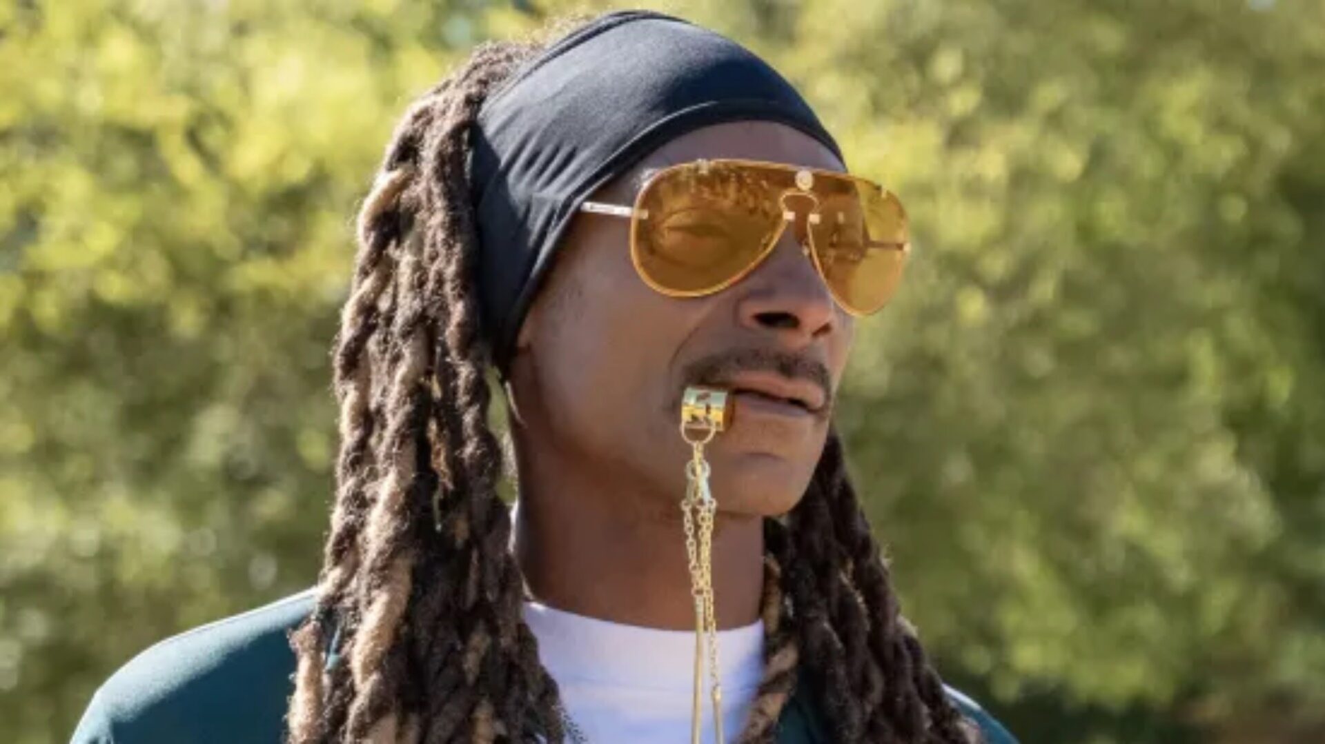 Snoop Dogg wearing yellow sunglasses, a bandana blowing a gold whistle