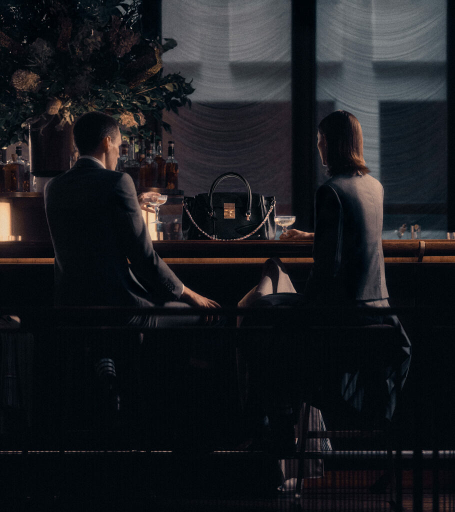 A lifestyle image of two models sat at a bar with the new Thom Browne Bolton Bag