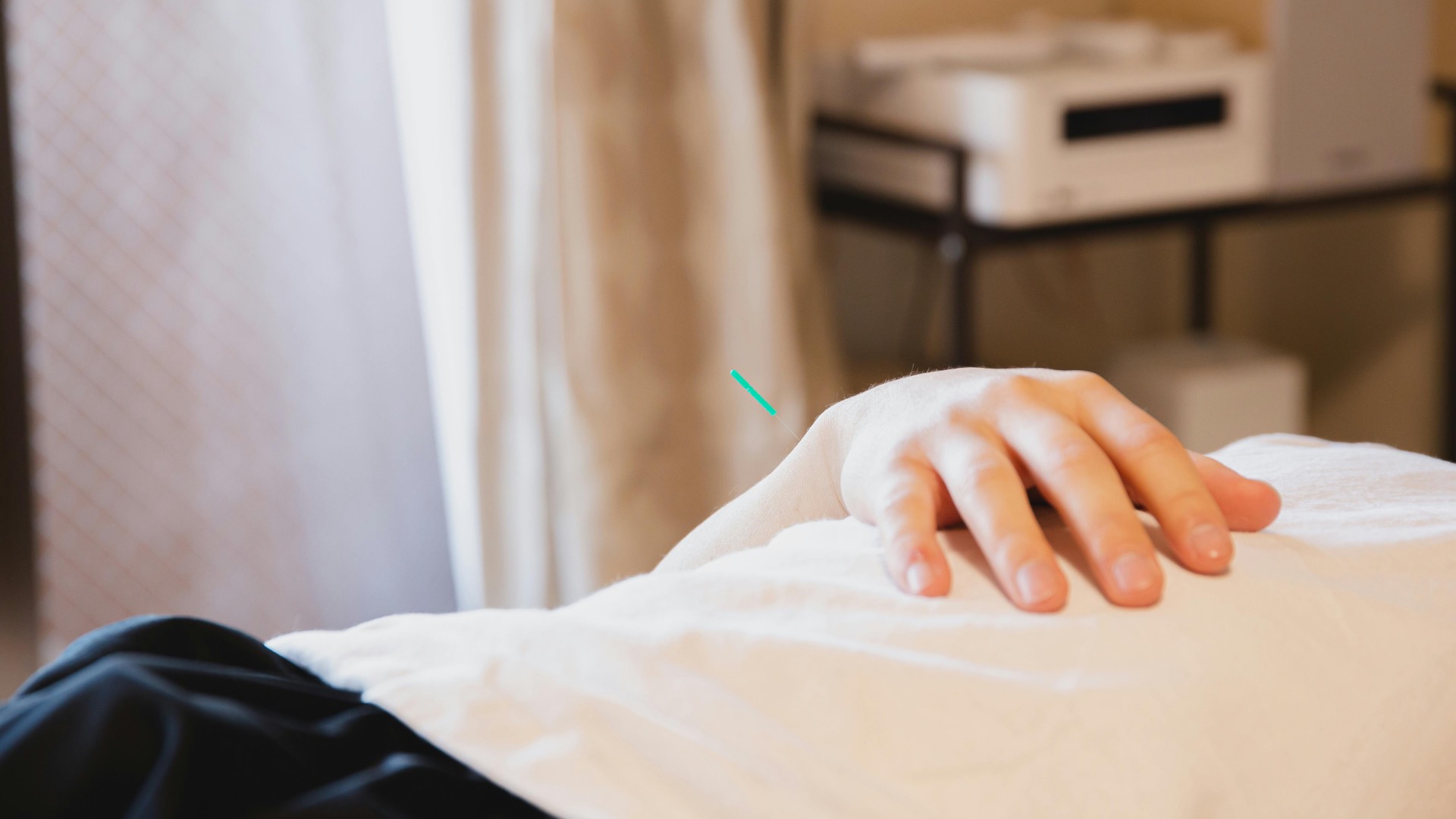 a person lying on a bed with a small pin in their hand, a curtain in the background