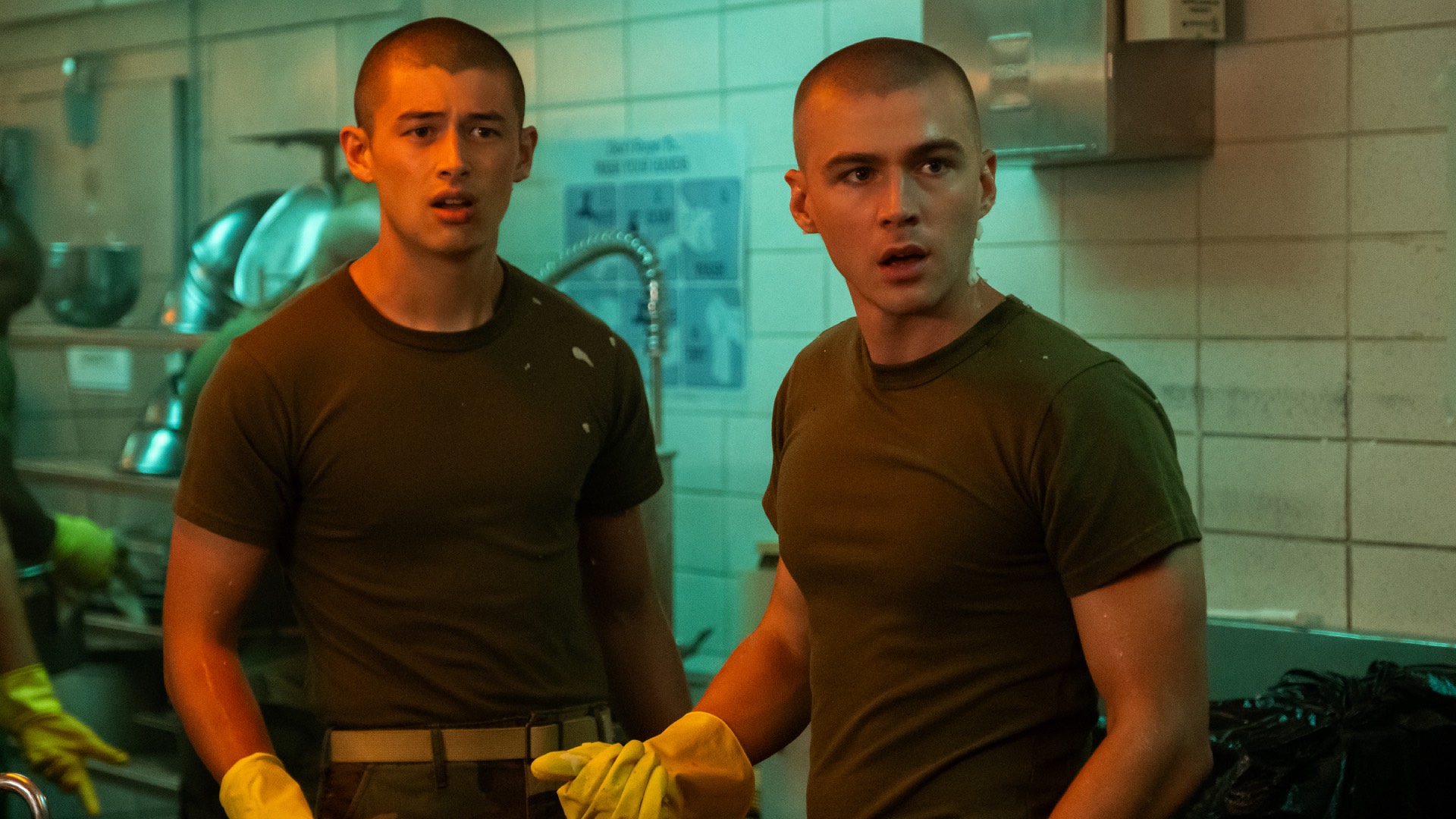 Liam Oh and Miles Heizer in Boots in character in green t-shirts, shaved heads, in yellow washing up gloves