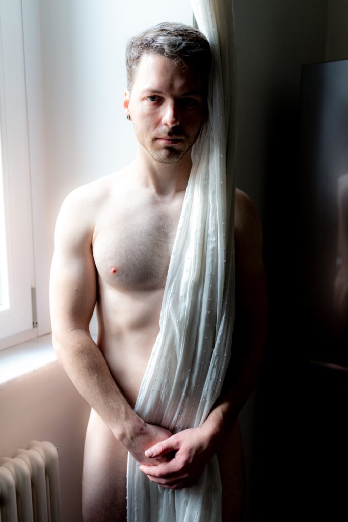Enea F topless standing behind a curtain by w window