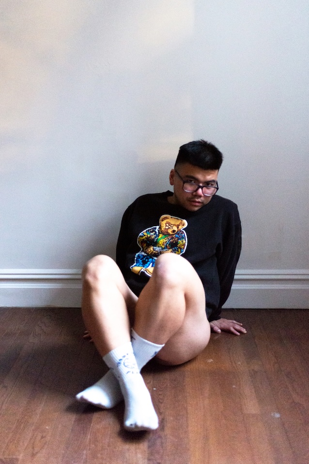 Kira S in a black sweater sitting down against a wall