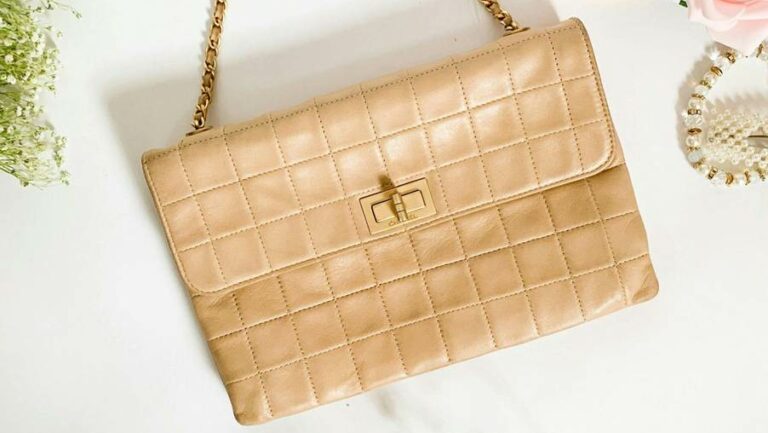 Close shot of a beige leather handbag with a gold strap