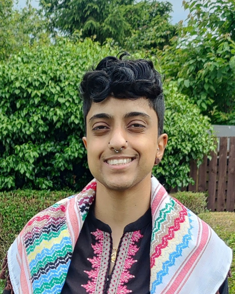 a head and shoulders shot of Maryam Din in a green garden with a patterned shawl over shoulders