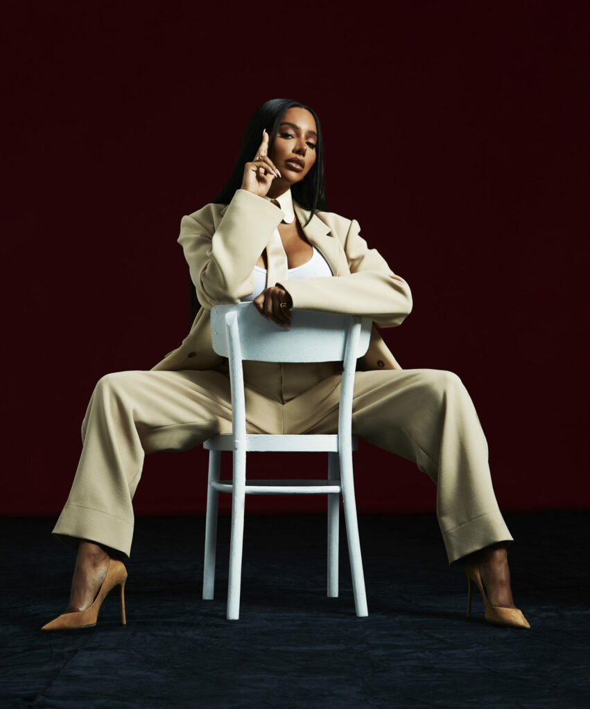 Munroe Bergdorf in a white suit sitting on a backwards chair