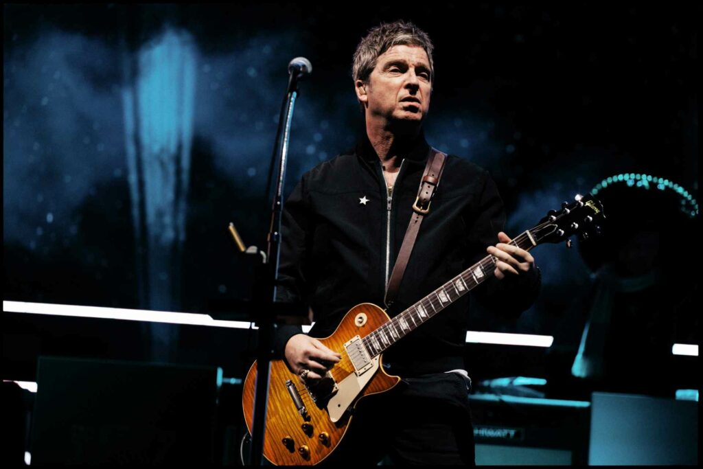 Noel Gallagher playing a guitar on stage at Wembley Stadium