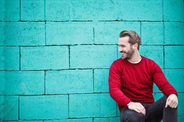 A smiling mna in a red top poses in front of a blue wall