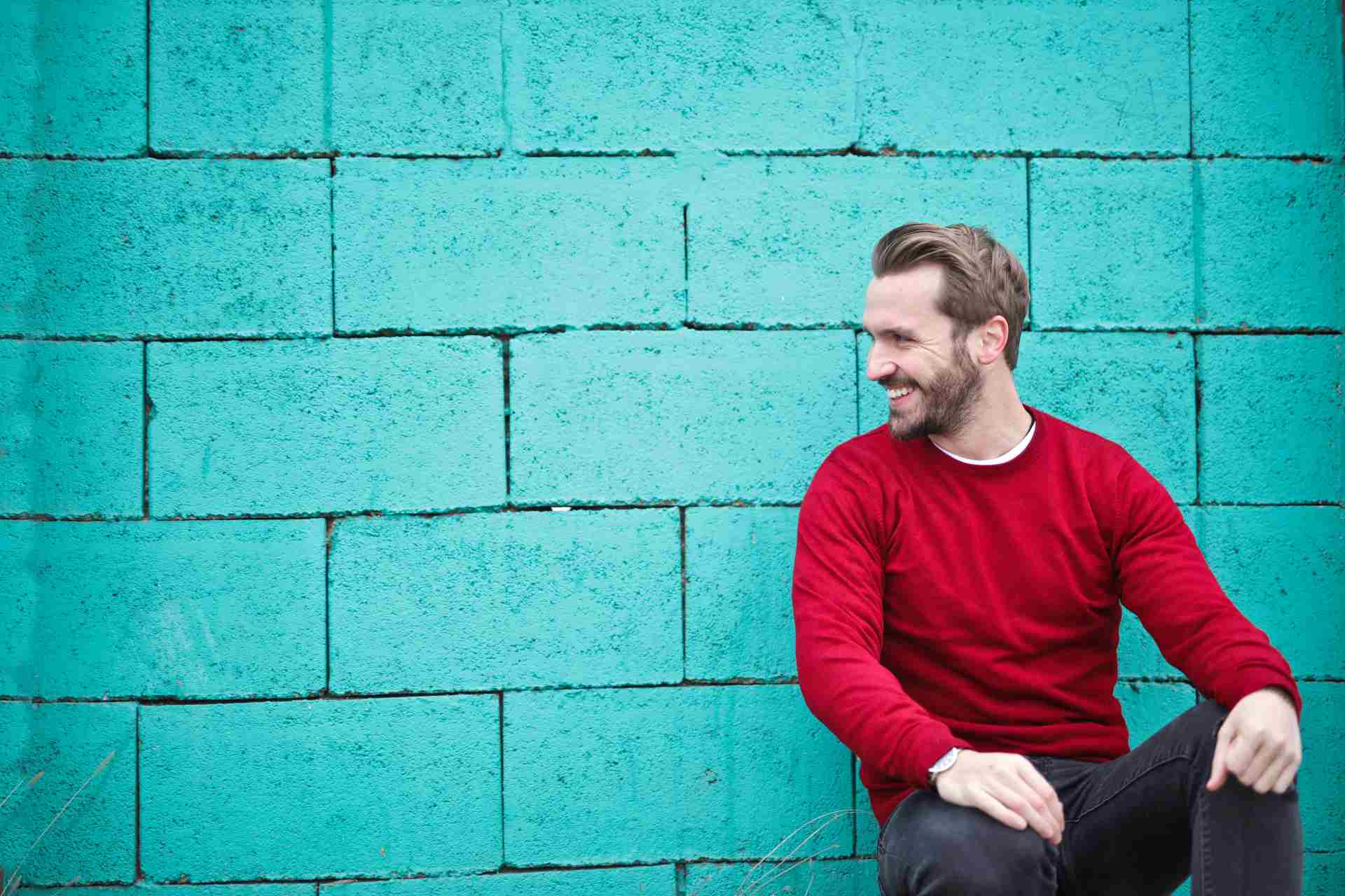 A smiling mna in a red top poses in front of a blue wall