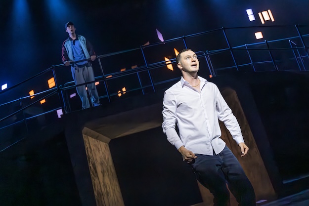 Man on stage with a man stood behind him on a balcony