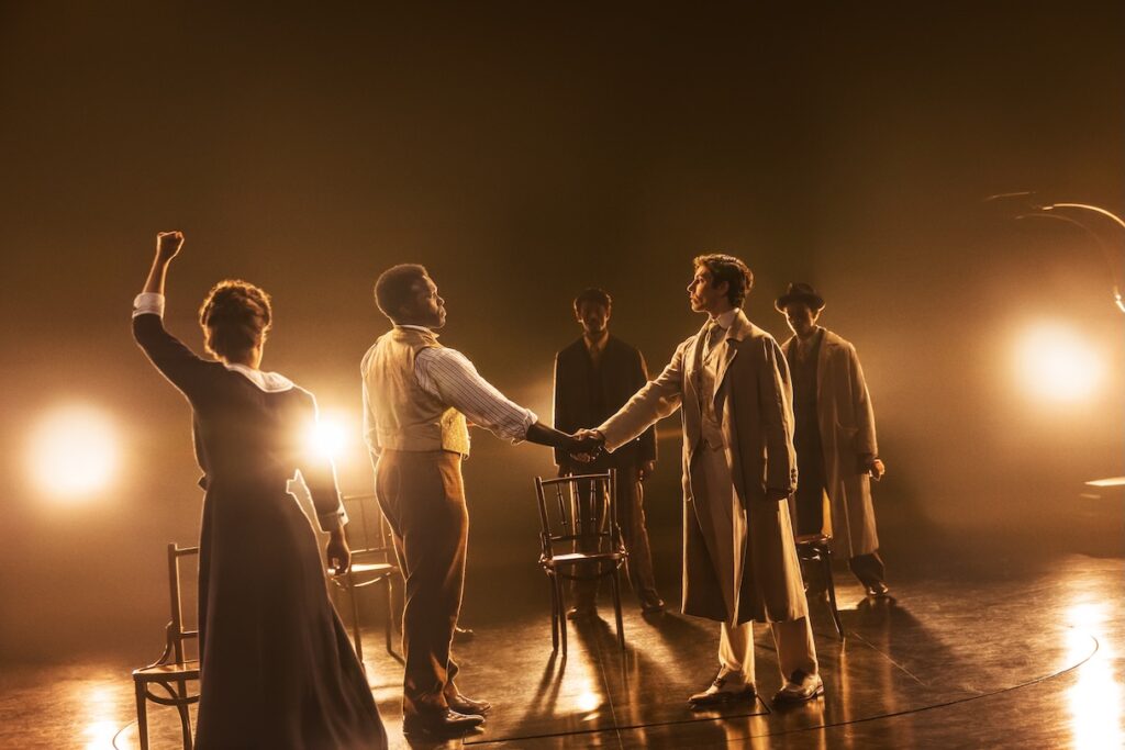 Cast of Ragtime lit up by golden light holding hands
