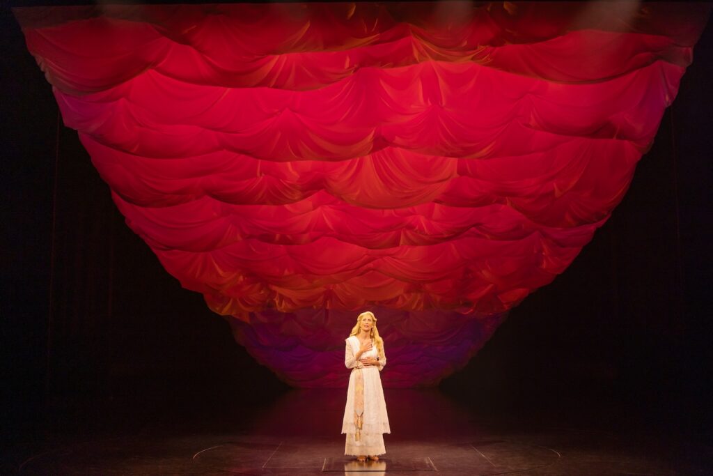 Woman alone on stage with a red backdrop