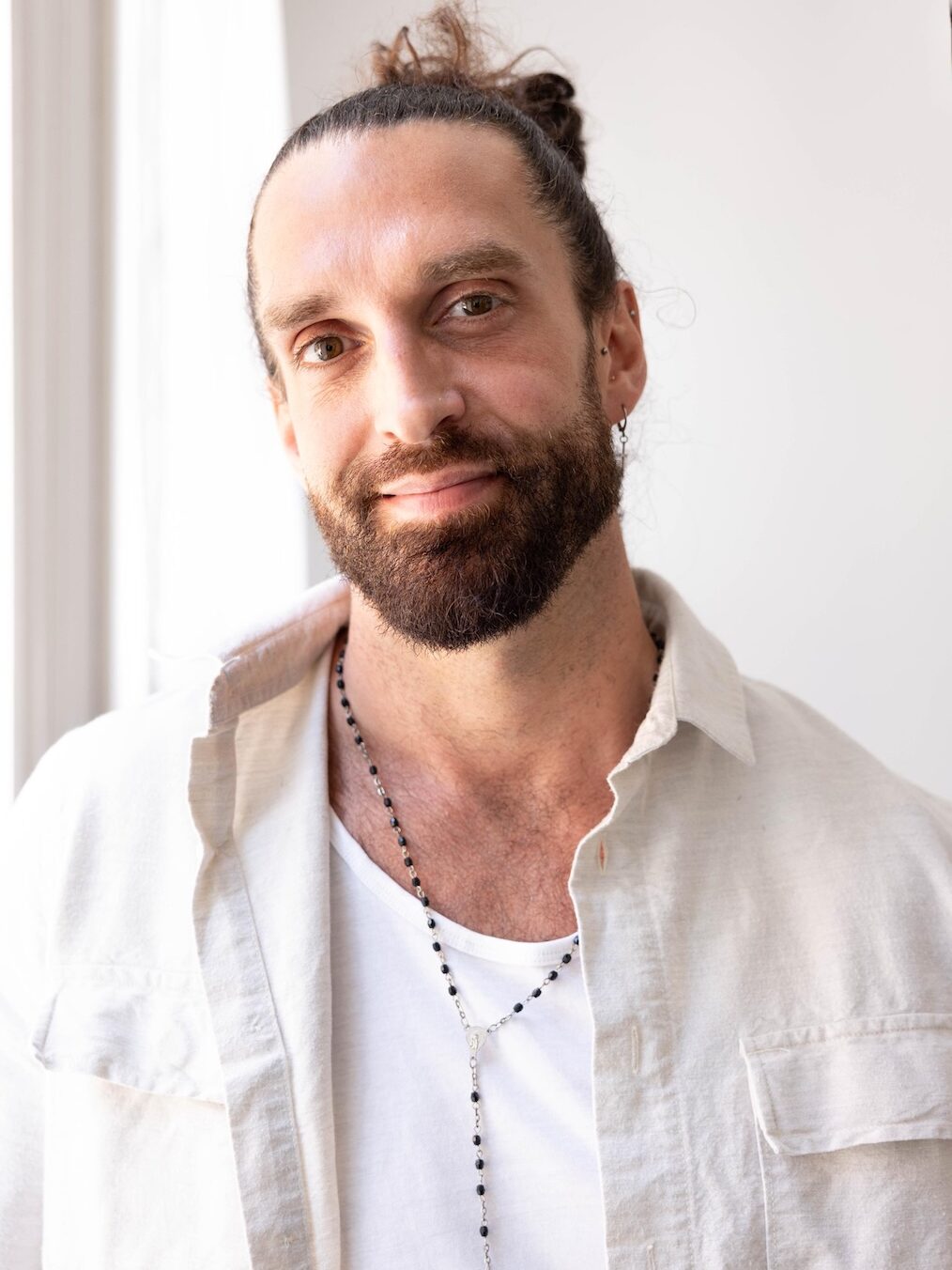 Andy Gardner in white t-shirt and cream jacket with a man bun