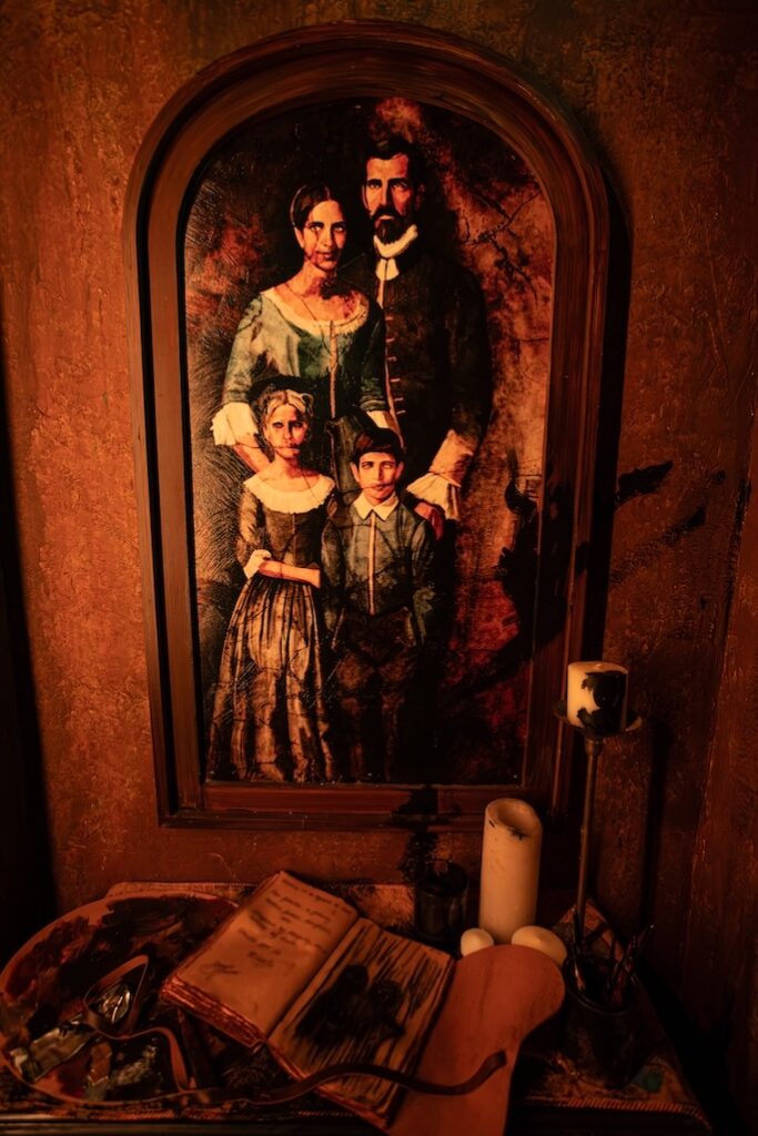 A scene inside El Artista: A Spanish Haunting including a painting of a family and a table with a book and a candle on it