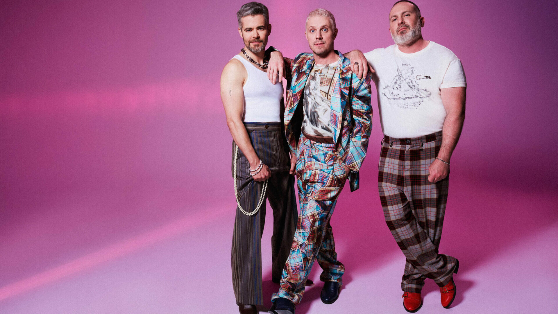 Scissor Sisters members standing together wearing Vivienne Westwood outfits against a purple backdrop