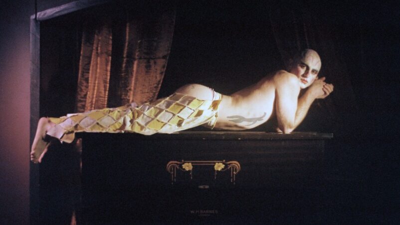 The artist NiCKY wearing a clown costume lying on a leather trunk