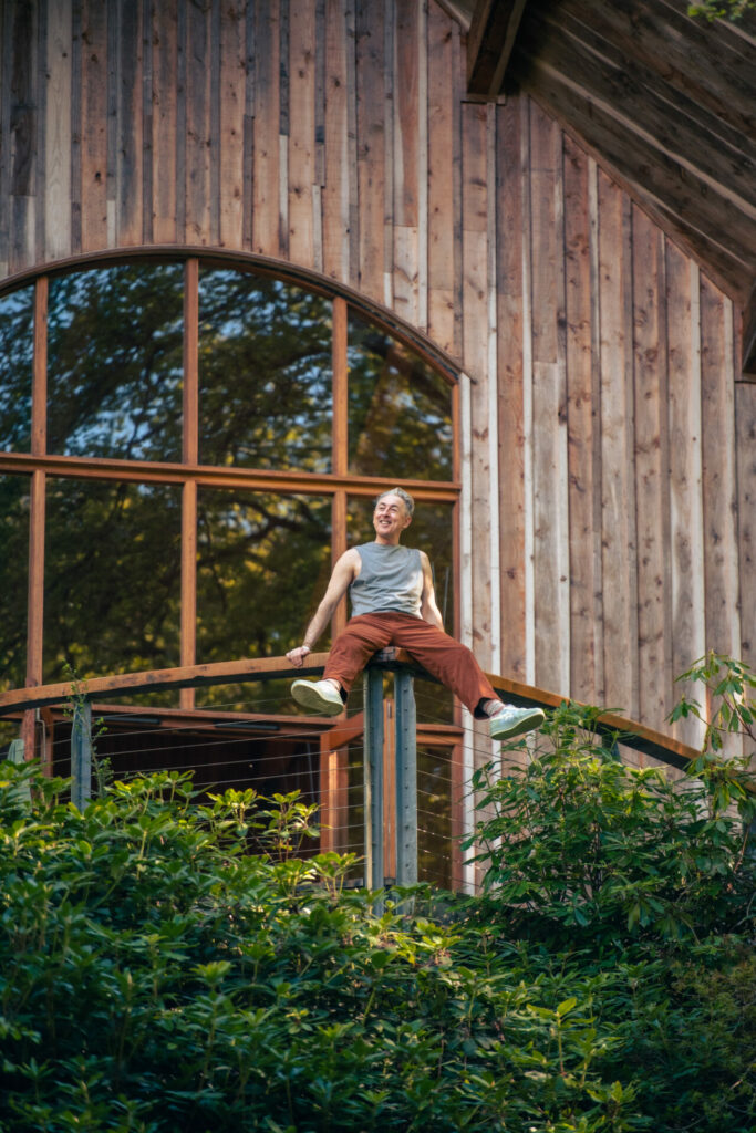 Alan Cumming outside a wooden building